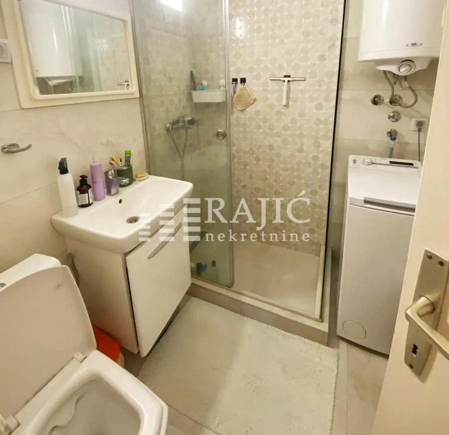 Smaller bathroom with a shower cabin, washbasin, and washing machine.