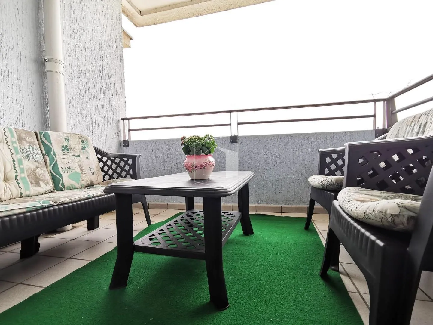 A balcony with outdoor seating and a green rug.