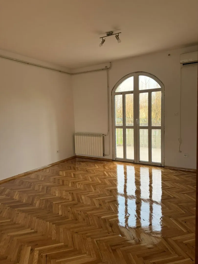 An empty room with glossy parquet flooring and a large arched balcony door.