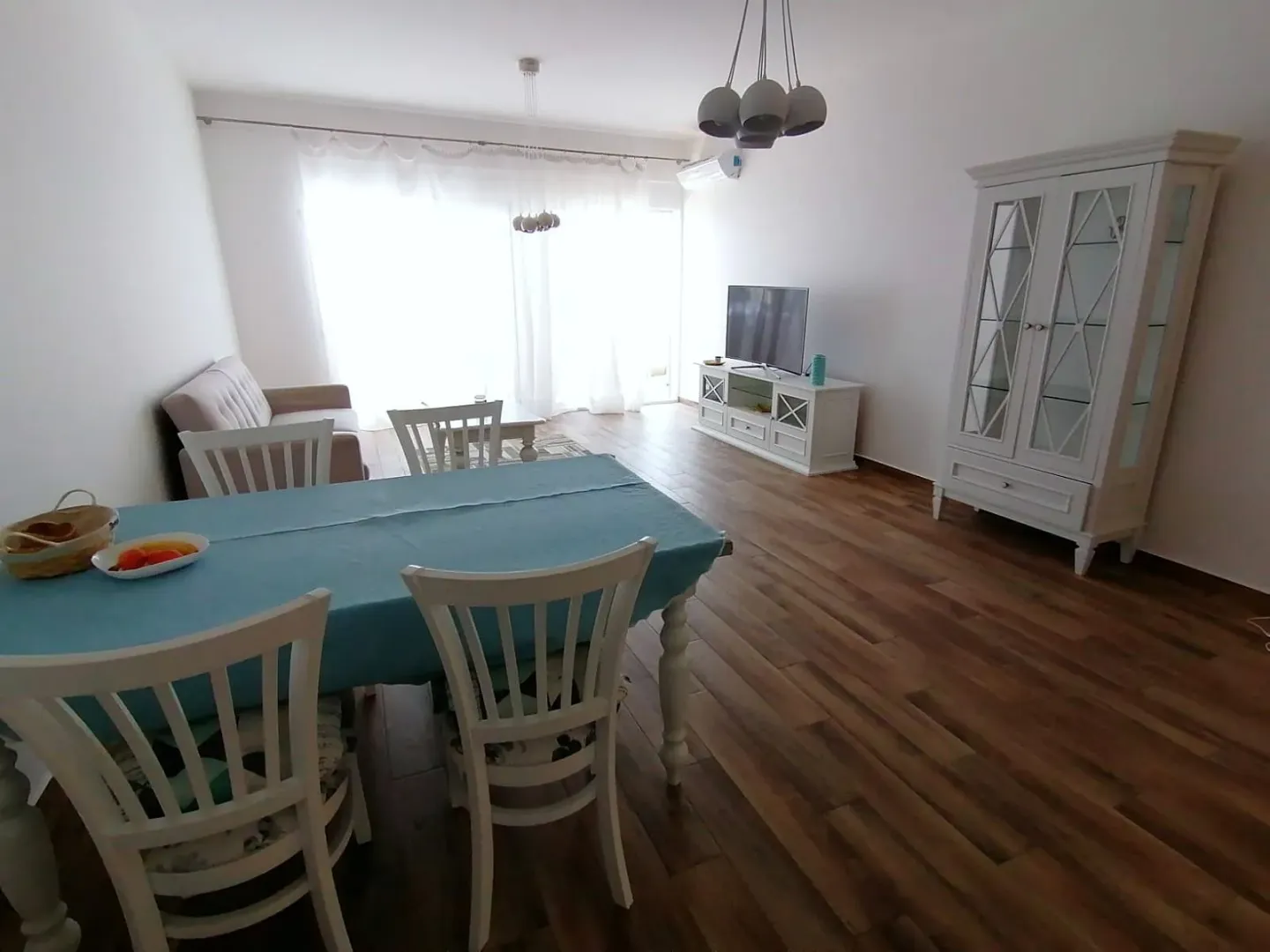 Dnevni boravak sa trpezarijom, kaučem, televizorom i bijelom vitrinom.