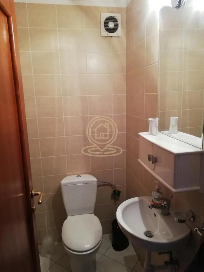 Manje kupatilo obloženo keramičkim pločicama sa toaletom, umivaonikom i ogledalom.