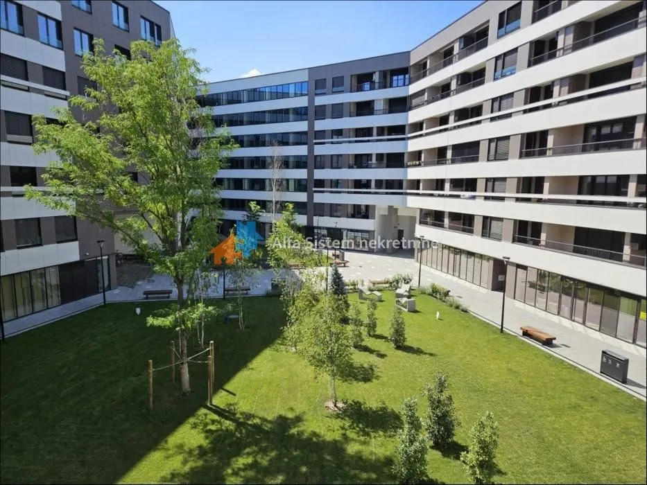 Unutrašnje dvorište sa zelenom površinom i stazama okruženo modernom stambenom zgradom.