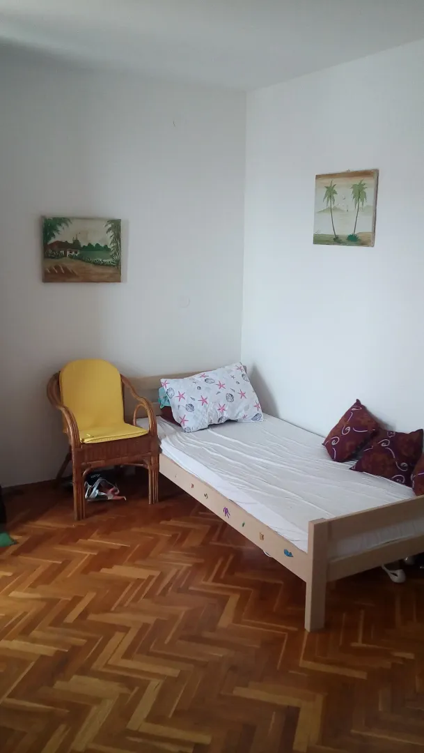 Manja spavaća soba sa krevetom, drvenom foteljom i parketom.