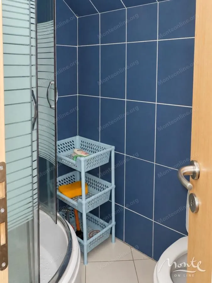 Smaller bathroom with blue wall tiles, shower cabin and shelves.