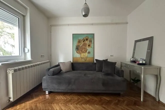 Dnevna soba sa sivom sofom, radnim stolom i umetničkom slikom na zidu.