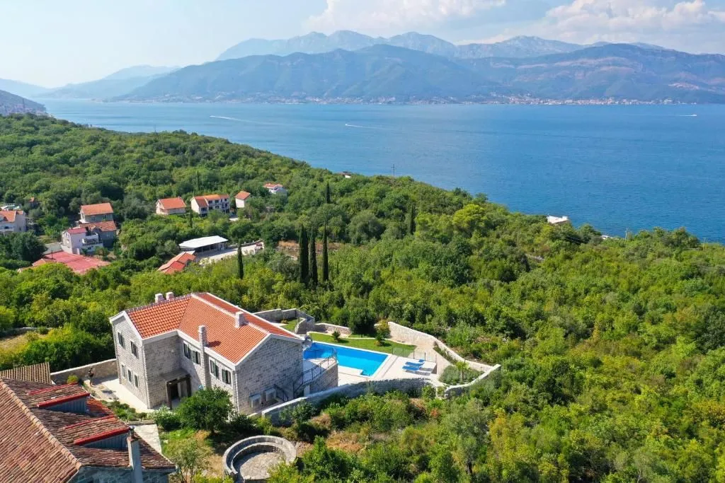 Aerial view of a stone house with a swimming pool near the sea.