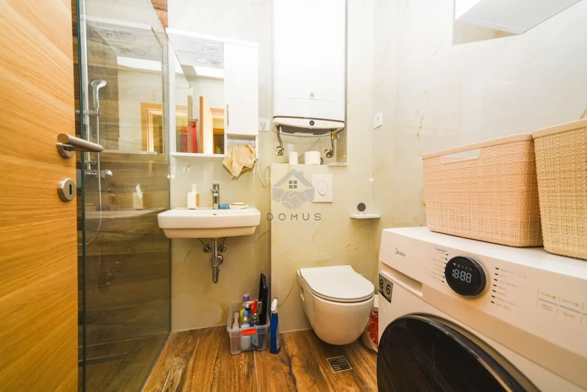Small bathroom with a shower cabin, washbasin, toilet, and washing machine.