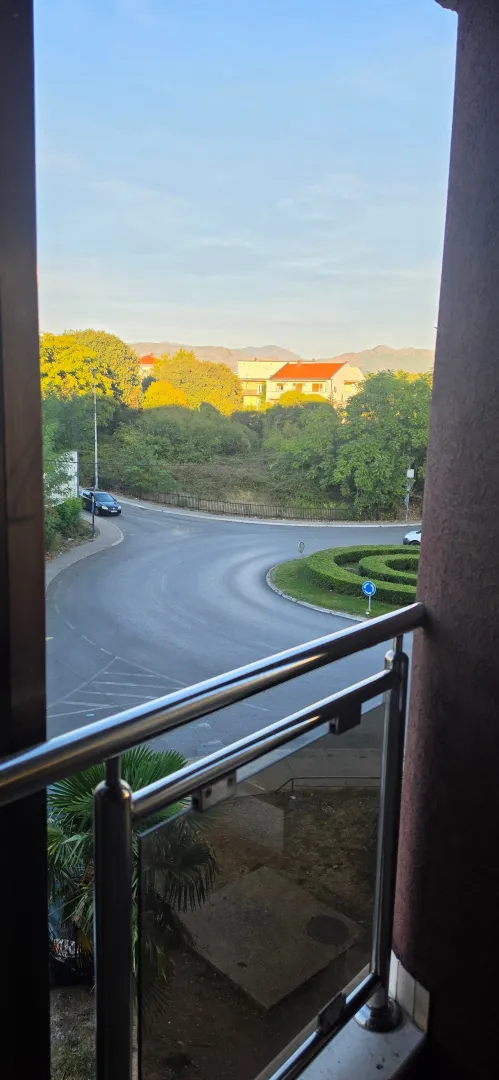 Pogled sa balkona na ulicu, zelenilo i okolne zgrade.