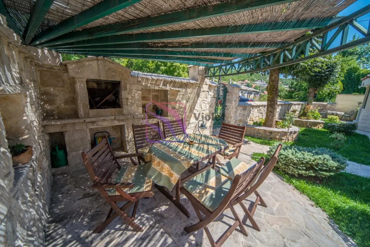 Natkrivena terasa sa kamenim roštiljem i garniturom za sjedenje u dvorištu.