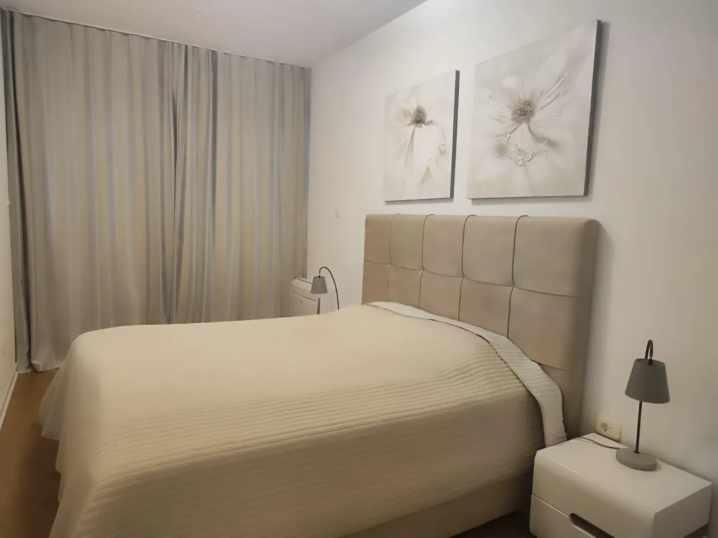 A bright bedroom featuring a double bed with decorative paintings above the headboard.