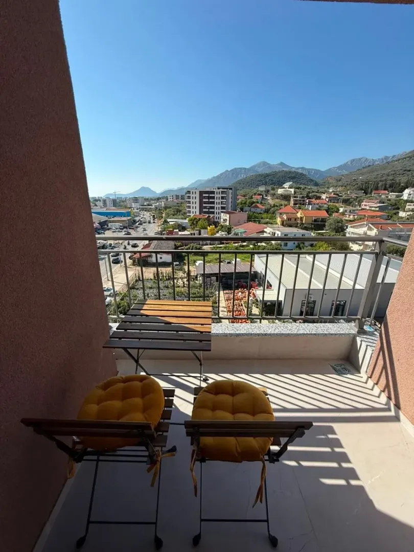 Small furnished balcony with a table, chairs, and a view of the surroundings and mountains.
