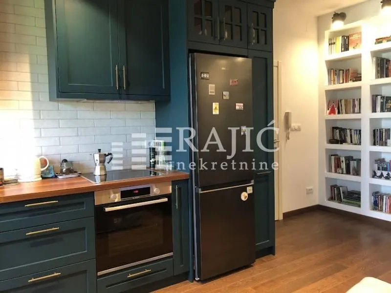 Modern green kitchen with built-in appliances and bookshelves.