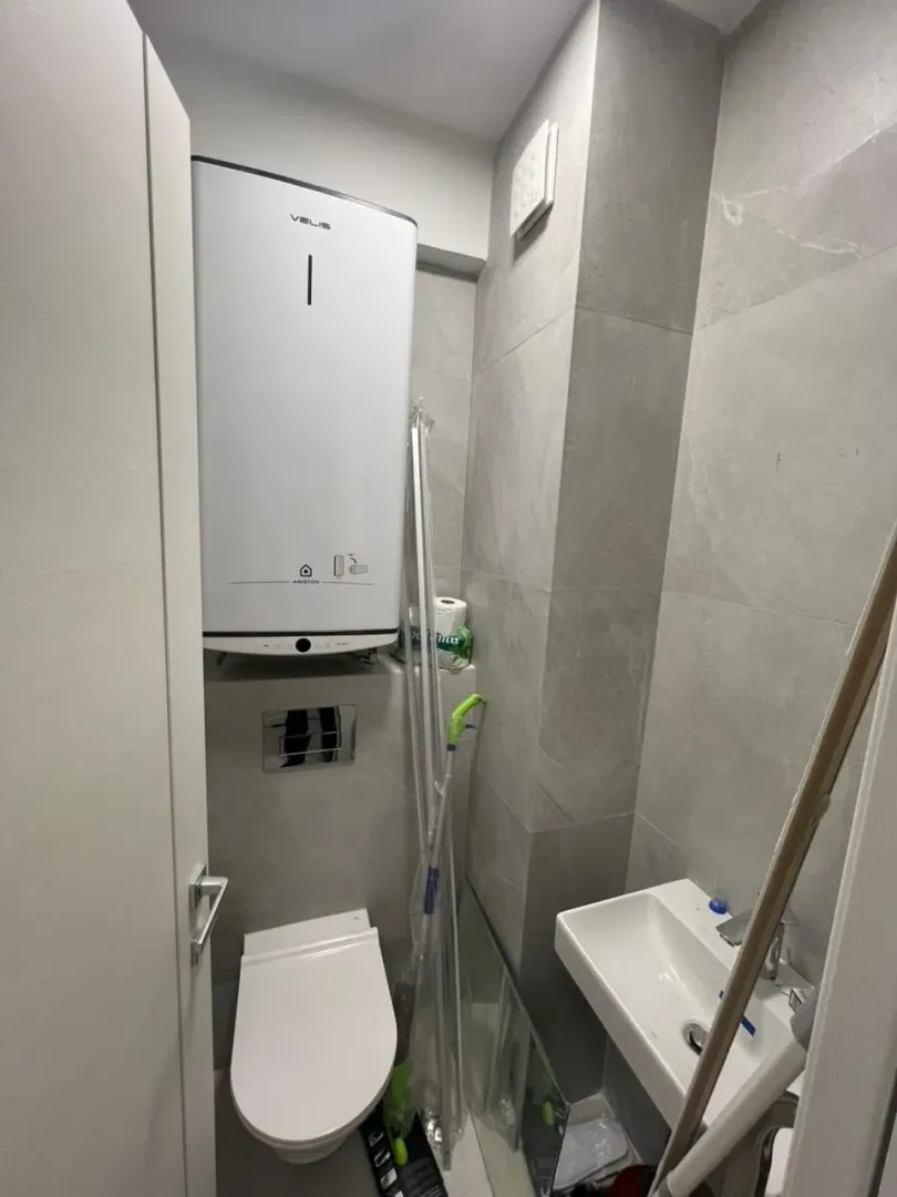 Small bathroom with a toilet, sink, and water heater on the wall.