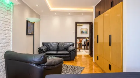 Living room with black leather furniture, parquet flooring, and a built-in wardrobe. - image 7