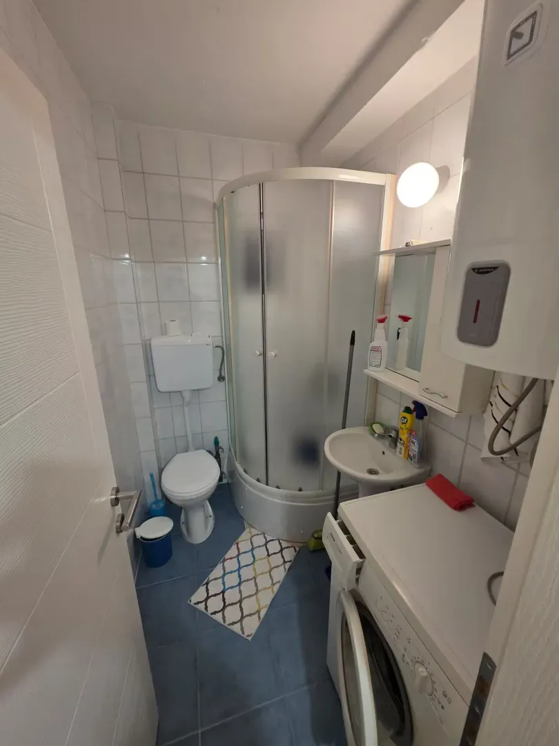 Manje kupatilo sa tuš kabinom, umivaonikom, WC šoljom i veš mašinom.