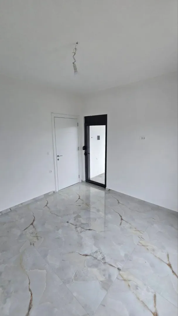 Prazna prostorija sa svijetlim keramičkim pločicama na podu i bijelim zidovima.