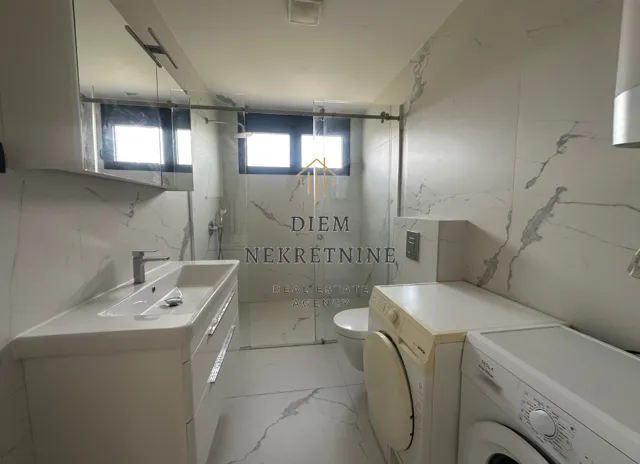 Modern bathroom with a walk-in shower, washbasin, and washing machine.