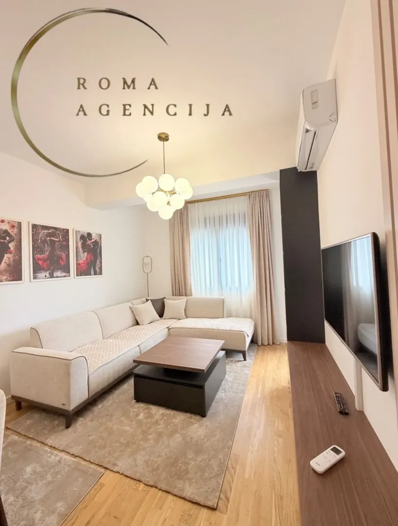 Dnevna soba sa ugaonom garniturom, stočićem i televizorom.