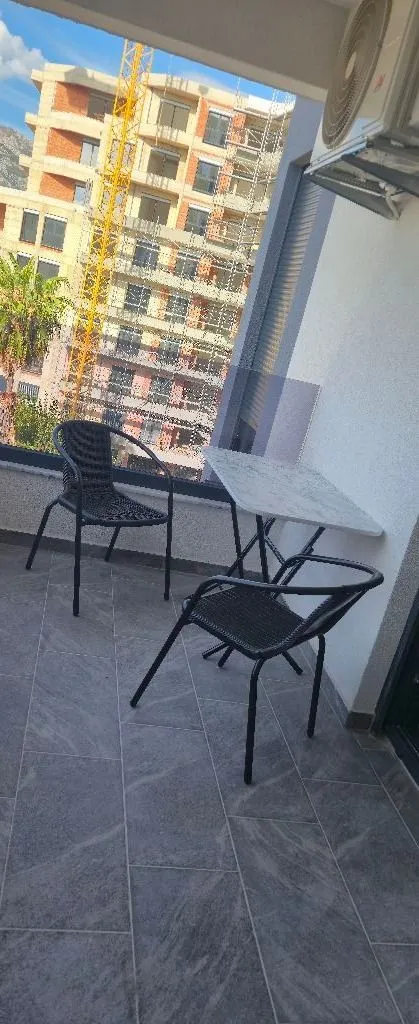 Furnished balcony with a table, chairs, and a view of a building under construction.