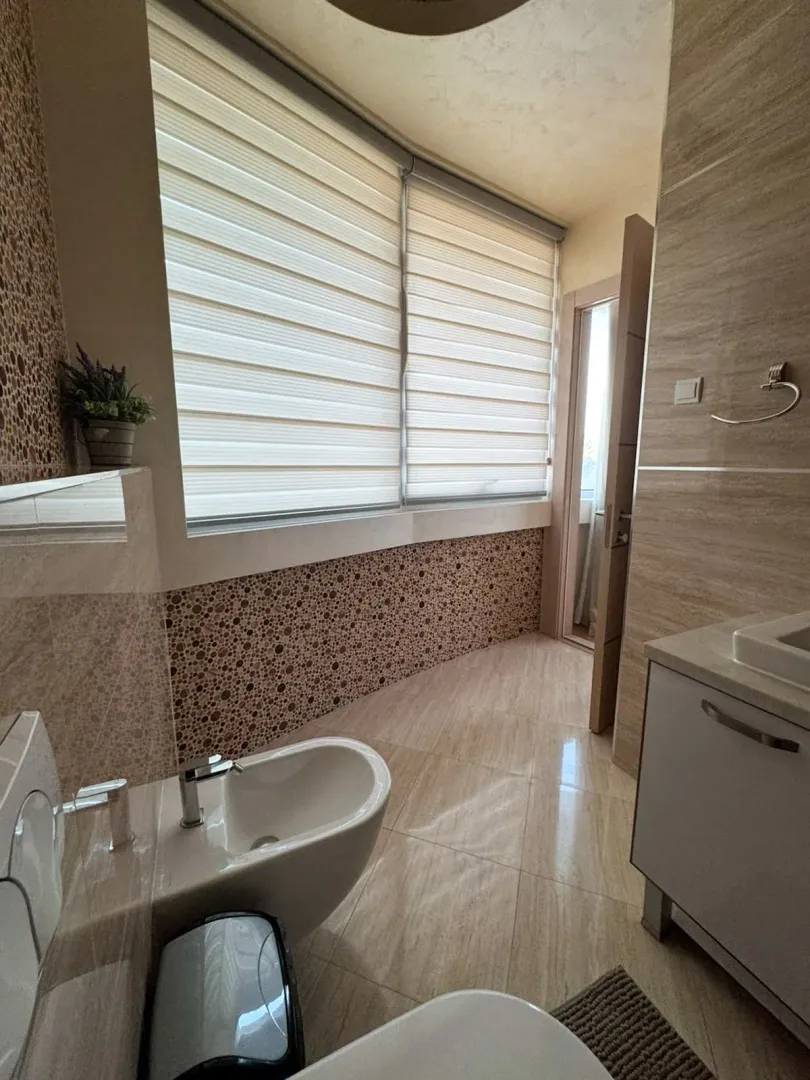 Moderne kupatilo sa bideom, lavaboom i velikim prozorom sa roletnama.