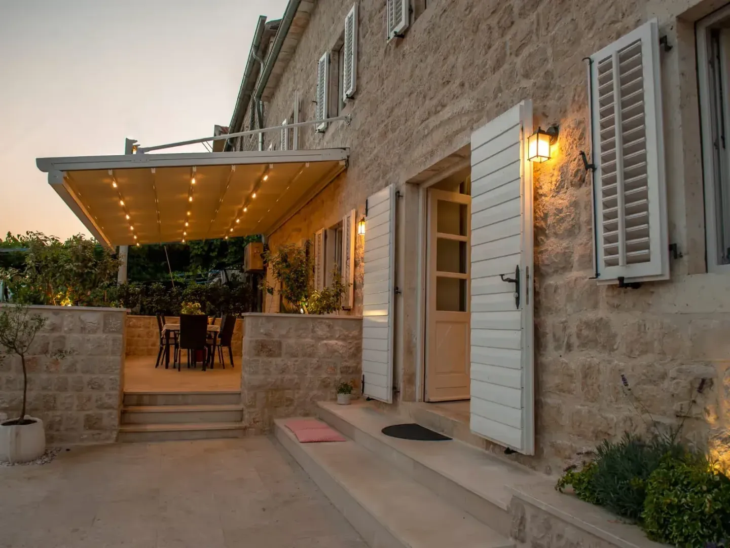 View of the stone house facade with an illuminated terrace and open doors.