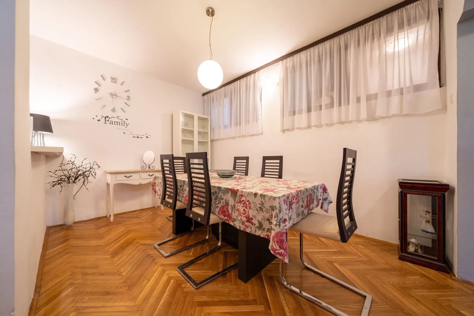 Dining room with a dining table and chairs, parquet flooring, and a decorative wall clock.