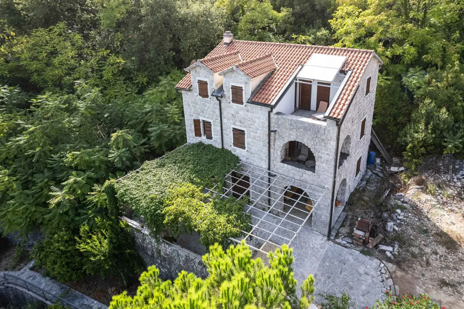 Pogled odozgo na kamenu kuću sa terasom i dvorištem okruženim zelenilom.