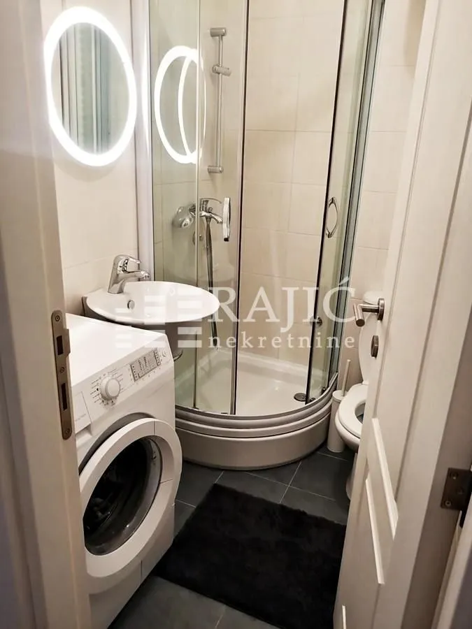 Smaller bathroom with a shower cabin, sink, and washing machine.