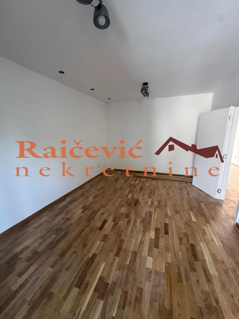 Prazna soba sa drvenim podom i belim zidovima.