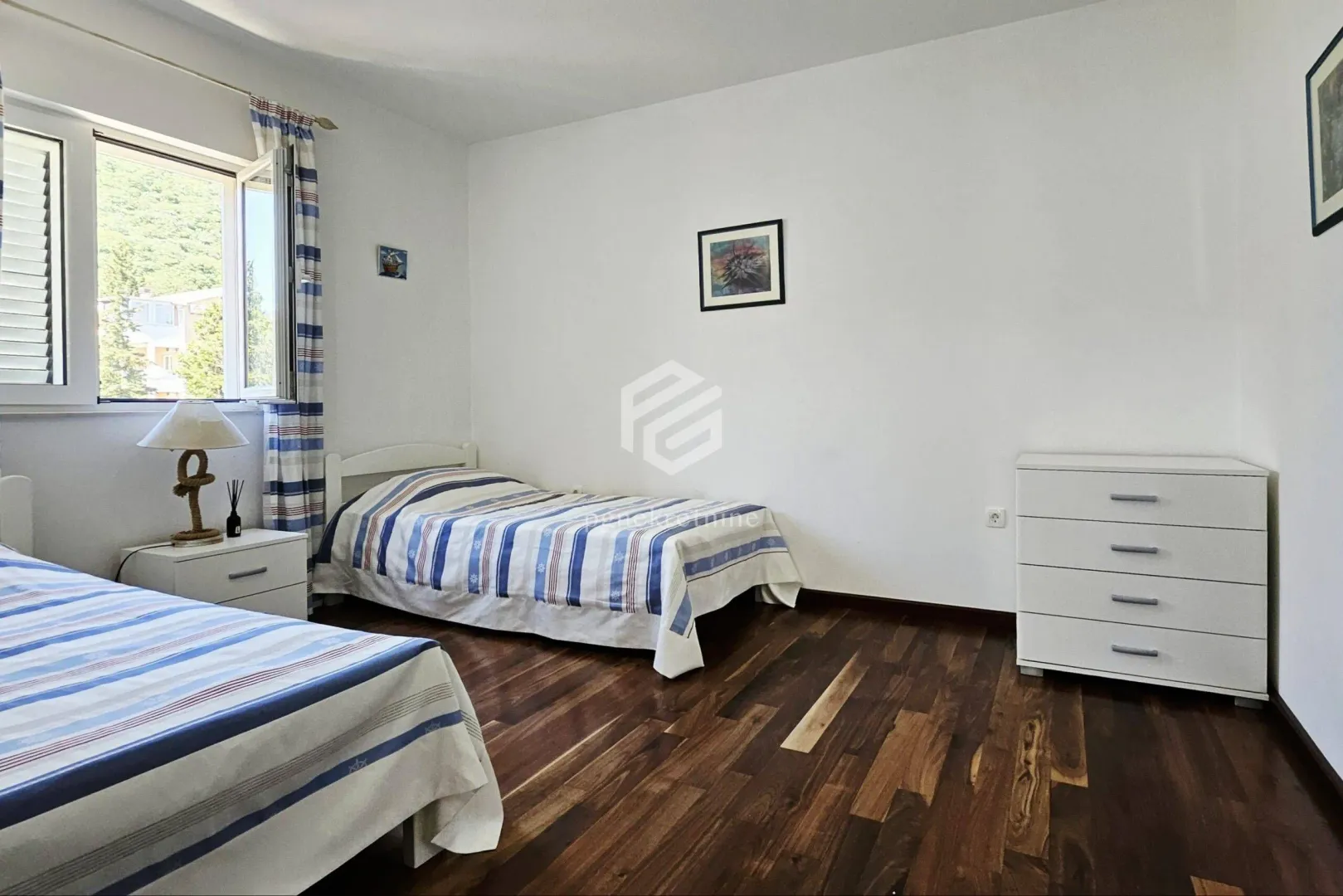 Spavaća soba sa dva kreveta, komodom i prozorom.