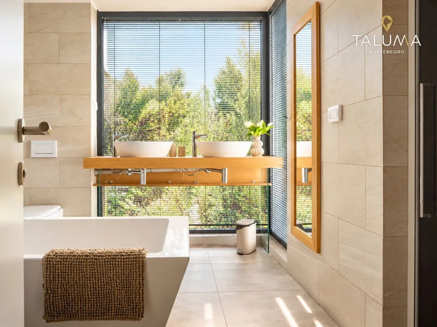Modern bathroom with a bathtub, double sink vanity, and a large window overlooking greenery.