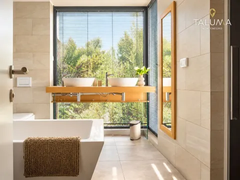 Modern bathroom with a bathtub, double sink vanity, and a large window overlooking greenery. - image 10