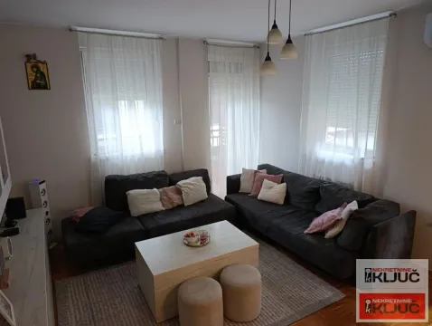Dnevna soba sa garniturom, stočićem i prozorima sa belim zavesama. - image 2