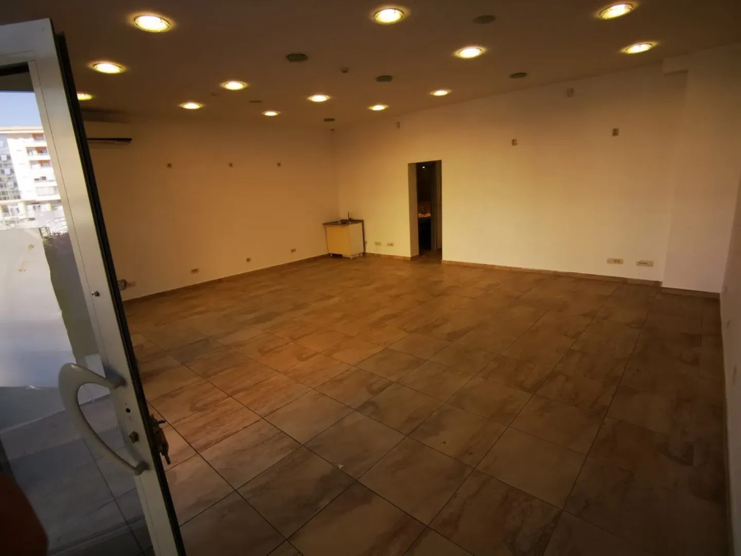 A spacious empty room with tiled floors and recessed ceiling lights.