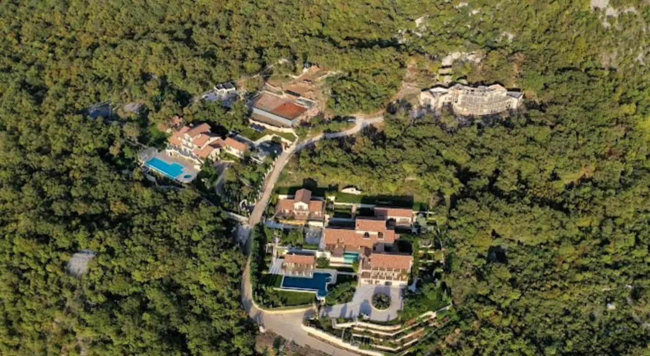 Pogled iz vazduha na kompleks kuća sa bazenima okružen šumom.