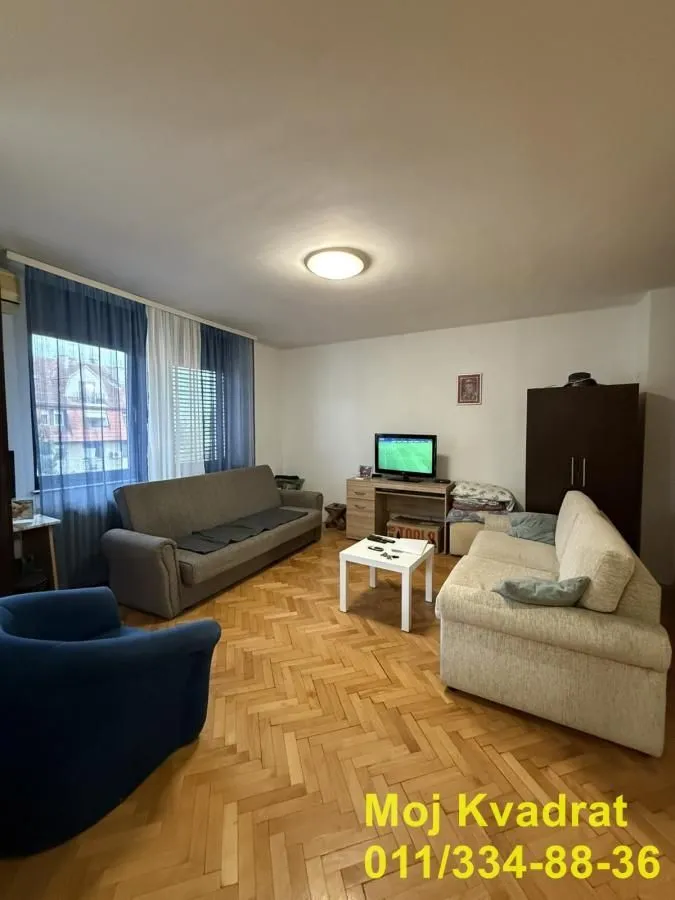 Dnevna soba sa garniturom za sedenje, parketom na podu i televizorom.