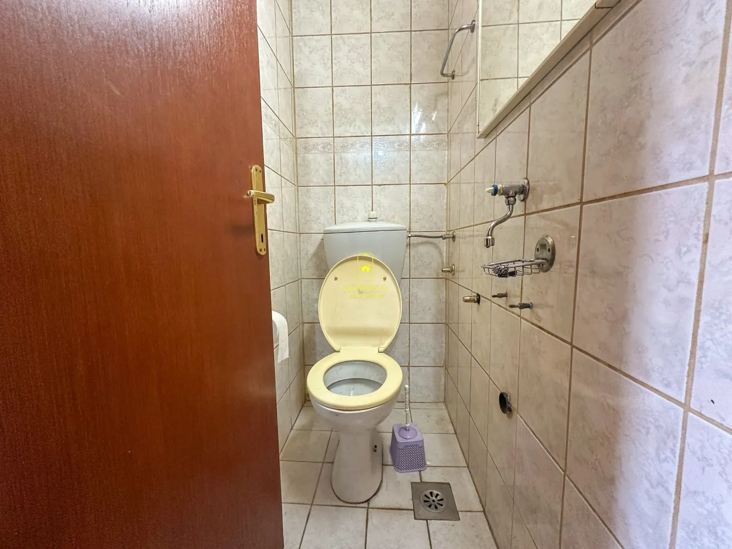 Manje kupatilo obloženo keramičkim pločicama sa šoljom i otvorenim drvenim vratima.