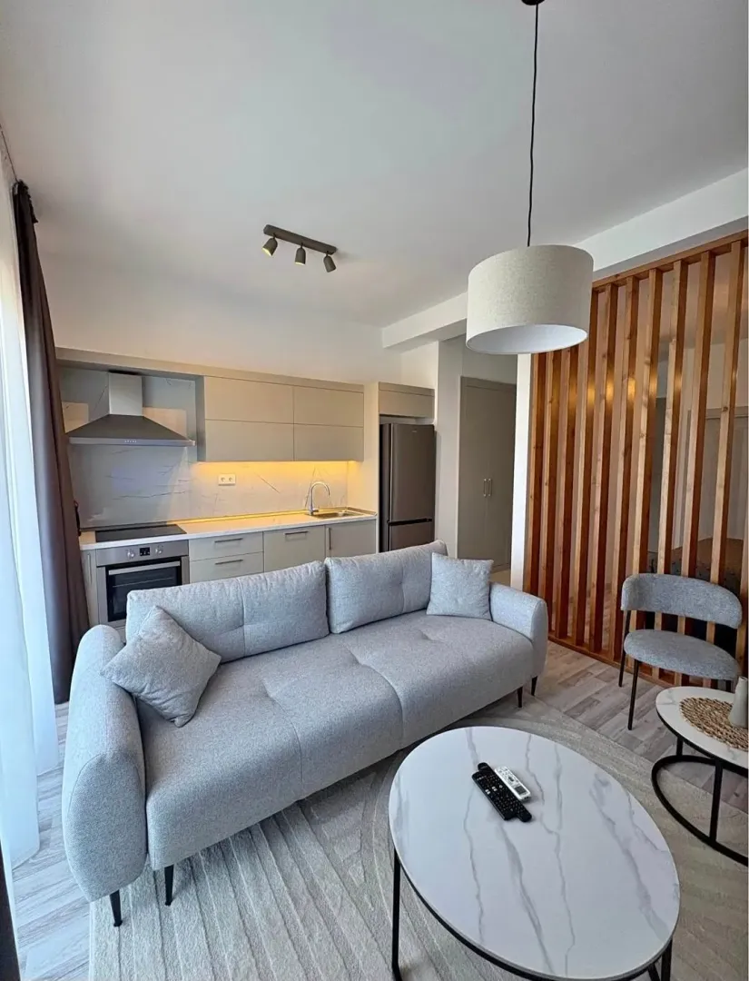 Modern living room with a sofa and an integrated kitchen in the background.
