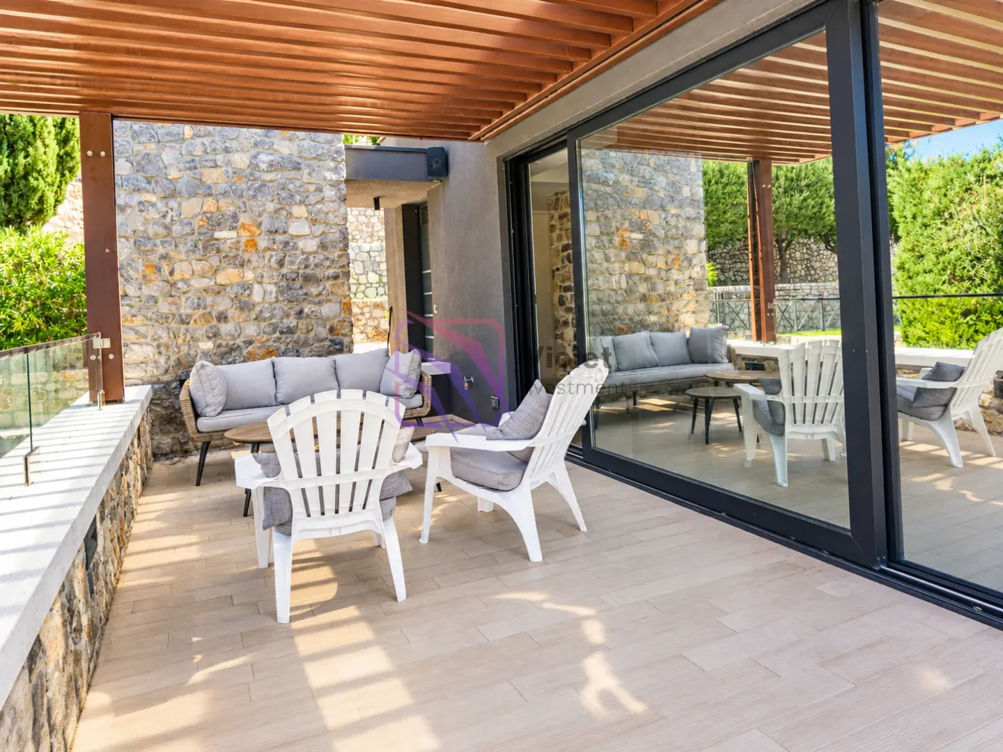 Covered terrace with seating furniture and a view of greenery.