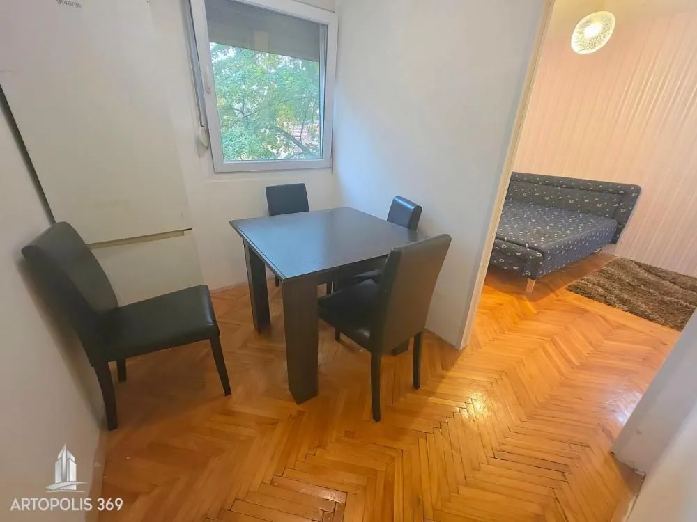 Dining area with a table, chairs, and refrigerator, with a view of another room.