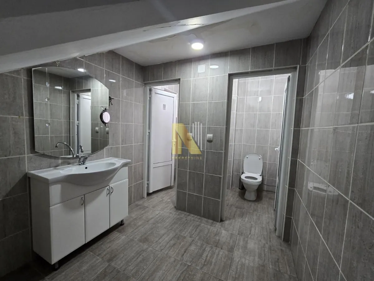 Tiled bathroom with a washbasin and a toilet in the background.