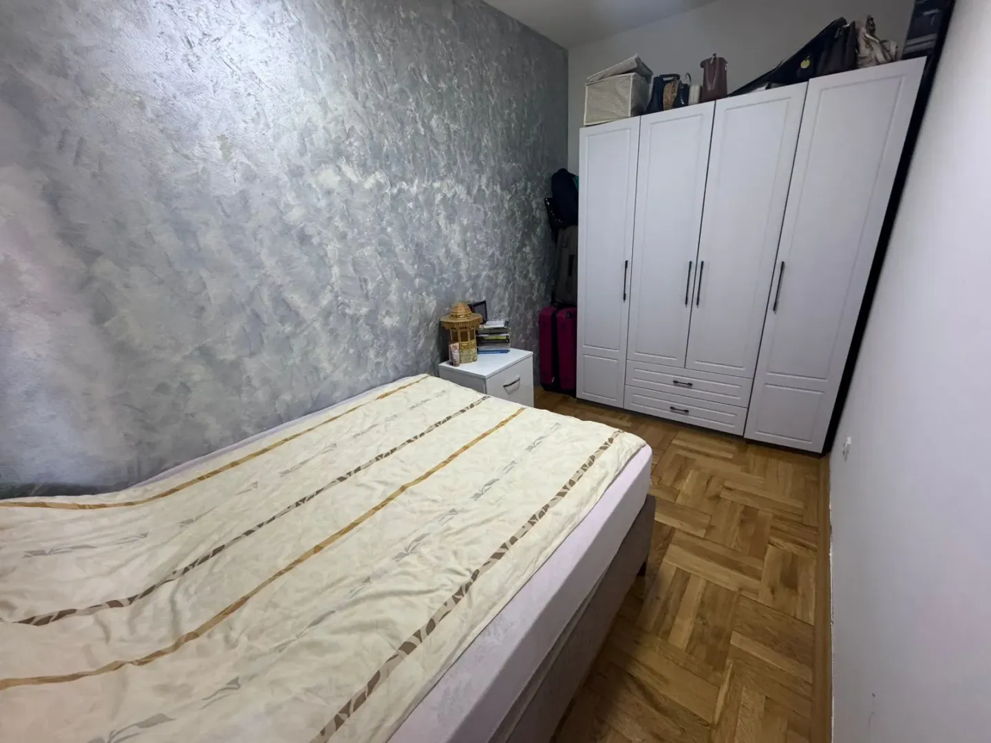 Bedroom with a bed, white wardrobe, and parquet flooring.