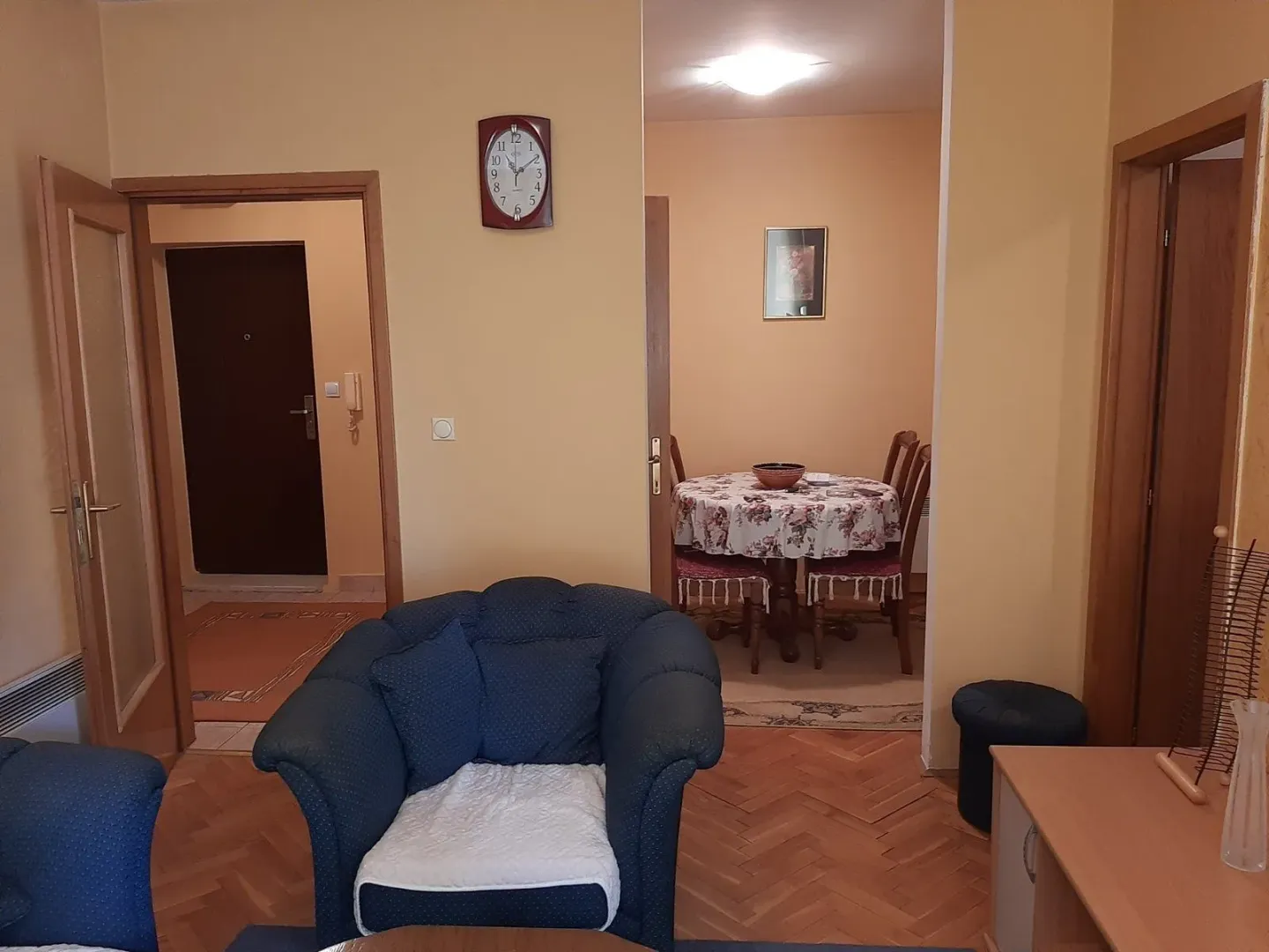 Dnevna soba sa foteljom i trpezarijom u pozadini.