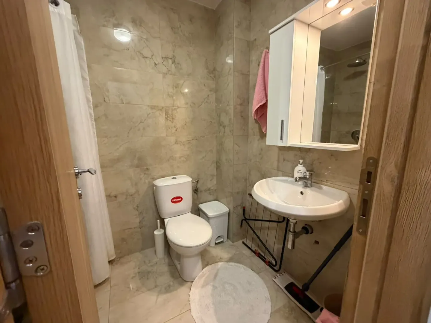 Manje kupatilo sa umivaonikom, WC šoljom i ogledalom sa ormarićem.