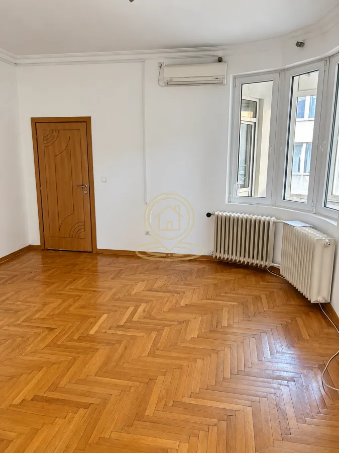 Empty room with wooden parquet flooring, a wooden door, and a window with radiators.