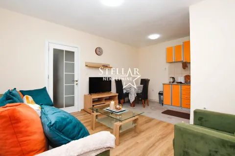 Living room with a sofa, TV, and kitchen in the background. - image 2