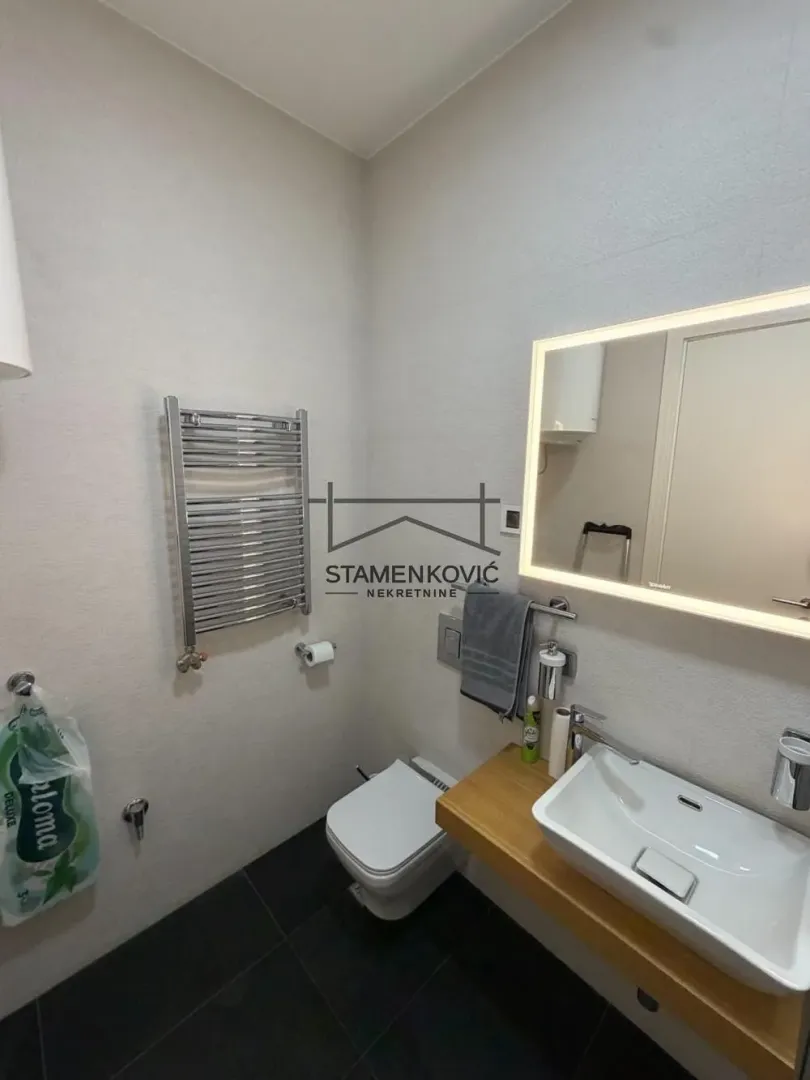 Savremeno opremljeno kupatilo sa umivaonikom, WC šoljom i ogledalom sa pozadinskim osvetljenjem.