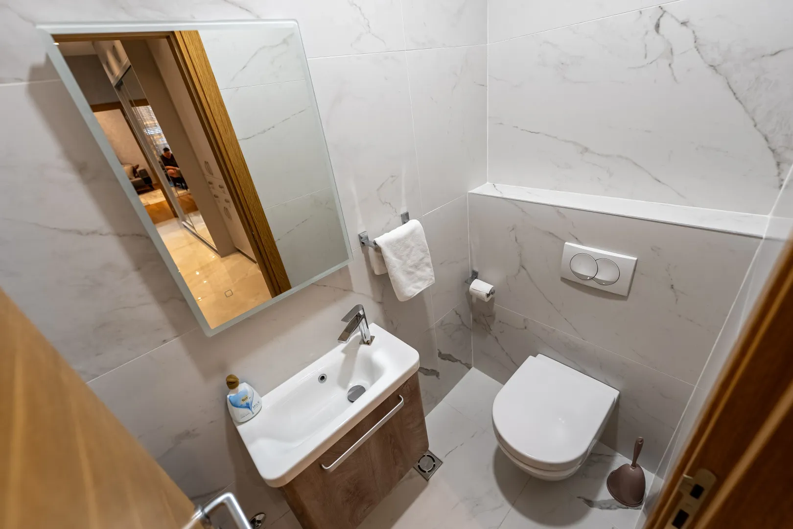 Modern bathroom featuring a basin, mirror, and toilet clad in marble tiles.