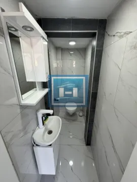 Small bathroom tiled with marble-effect tiles featuring a washbasin and toilet. - image 6