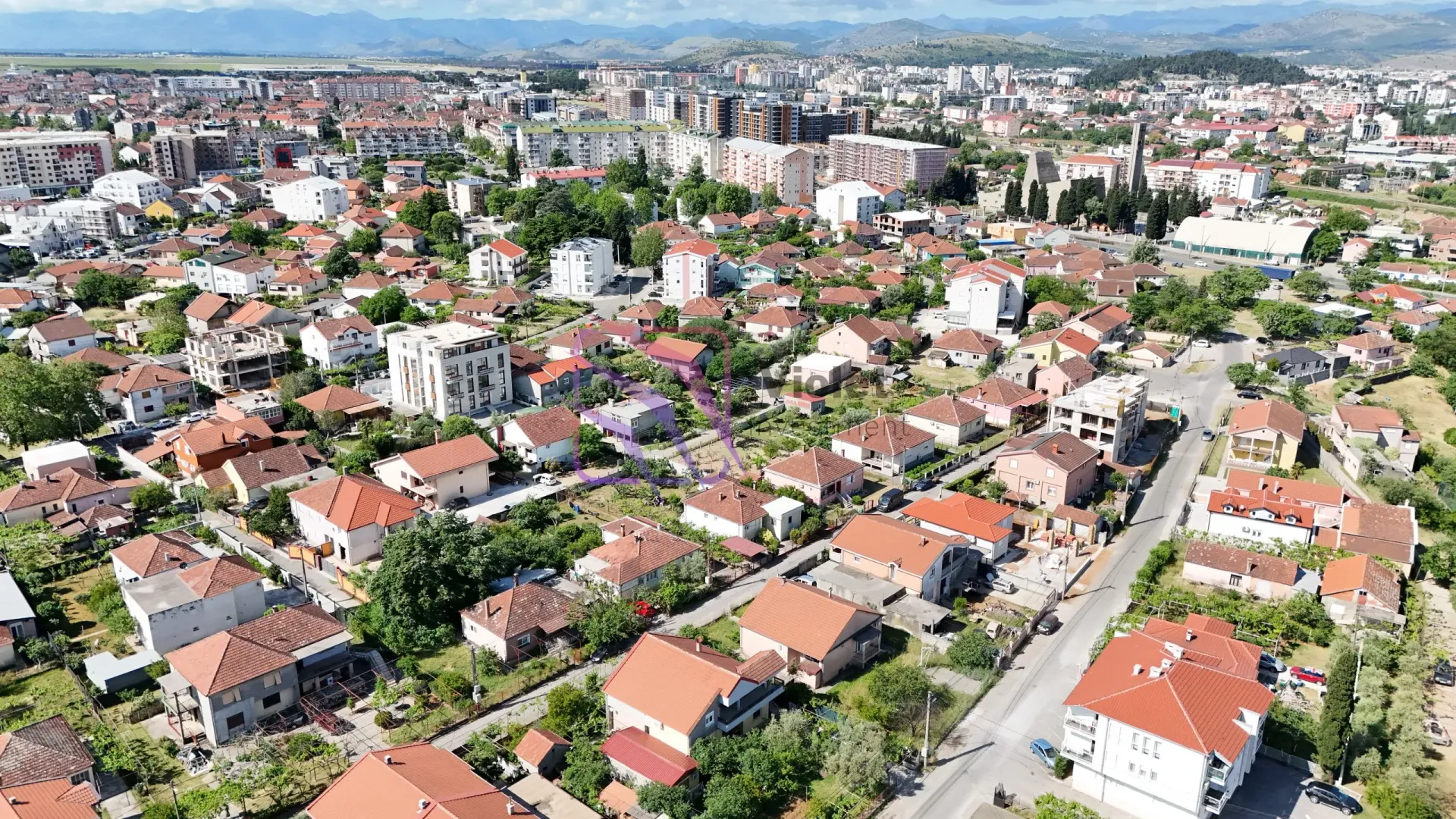 Pogled iz vazduha na gradsko naselje sa porodičnim kućama i zgradama u pozadini.